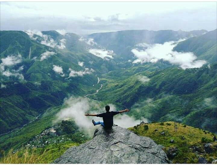 A trekker looking out over a stunning green valley and rolling hills in Meghalaya